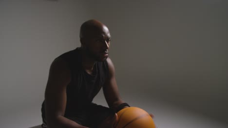 studio shot of seated male basketball player with hands holding ball 4