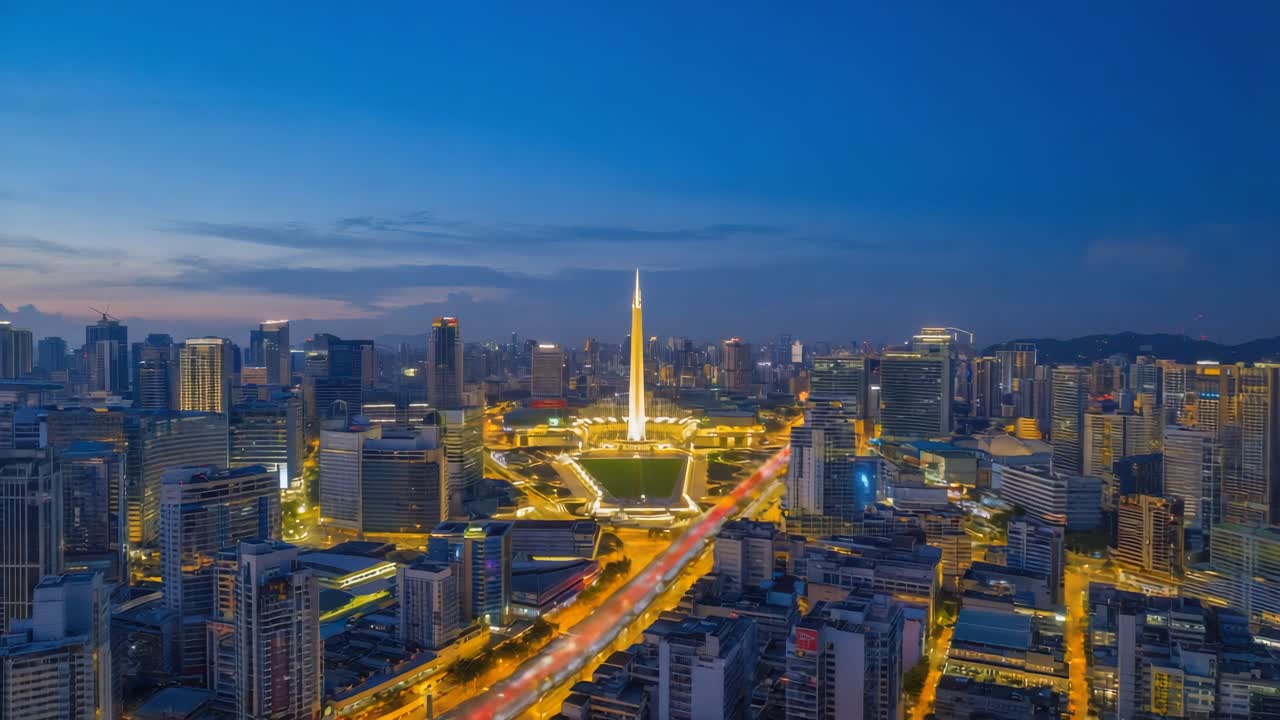 Nighttime panoramic view of a modern cityscape with illuminated skyscrapers and a central monument