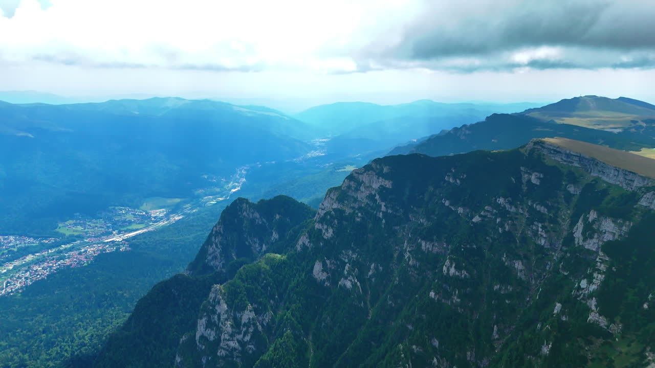 Footage over the high rocks close to the moving clouds. Aerial perspective on the village located in the valley from in the Bucegi Mountains, Romania