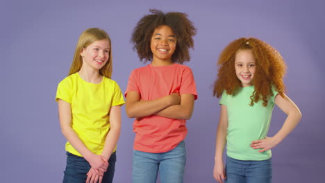 retrato de estudio de tres niños amigos de pie contra un fondo púrpura