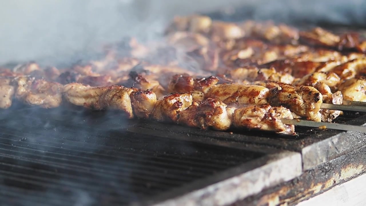 Spiedini di carne che grigliano su carboni ardenti con fumo che sale.