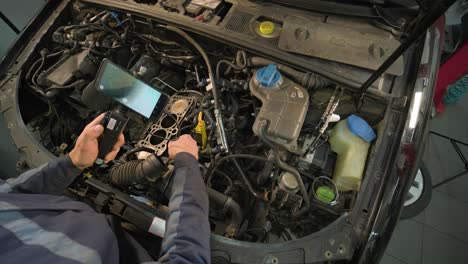 hands of car mechanic check the vehicle engine with technical endoscope with rotary camera and mobile phone. repair of engine head and valves.