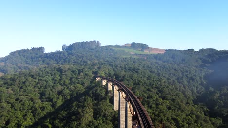 vista aérea de la vía del puente ferroviario alto a través de un valle hacia una colina con bosque nativo bajo la niebla de la mañana