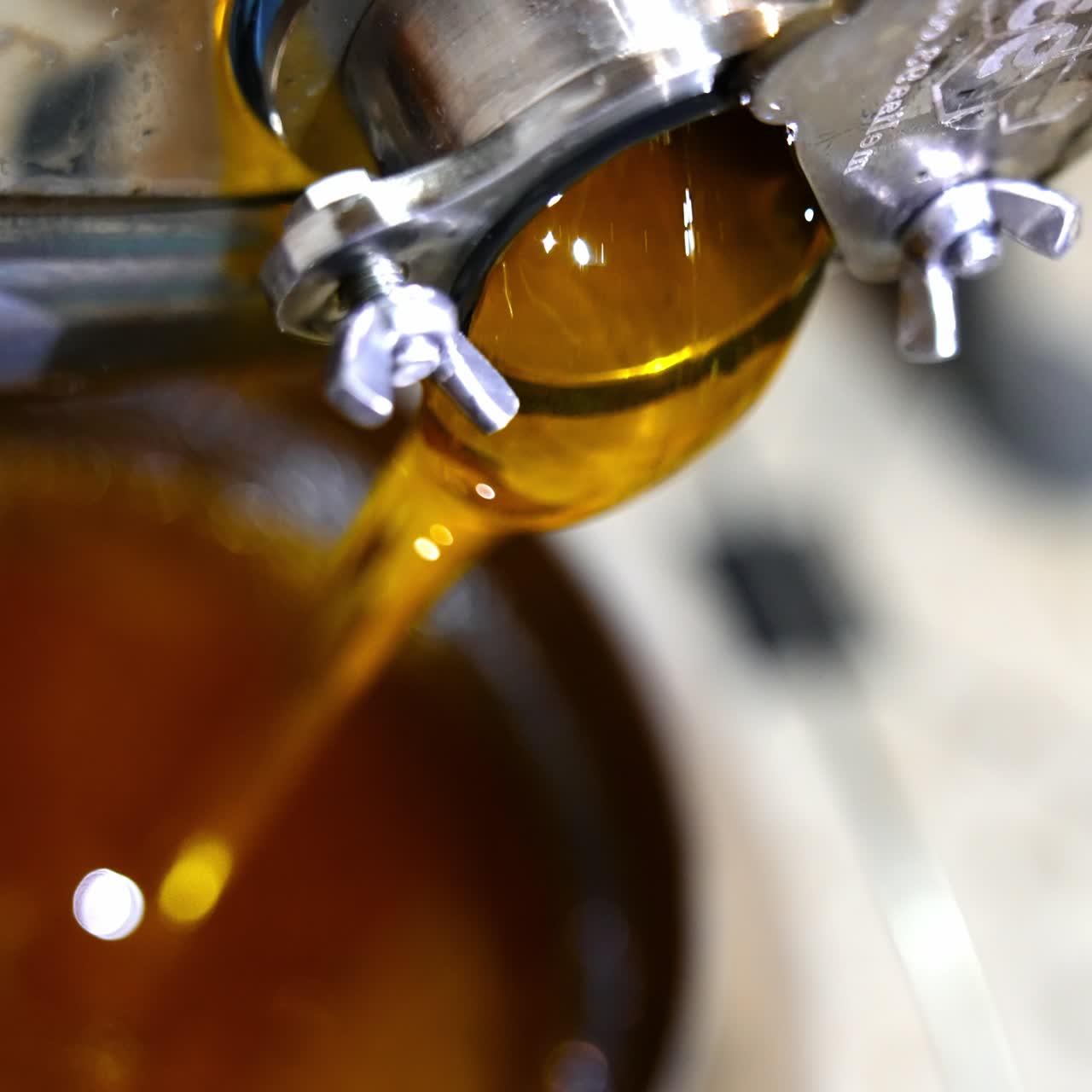Freshly extracted amber honey flowing from the mouth of a machine. The bucket is filled with organic product. Close up. Top view