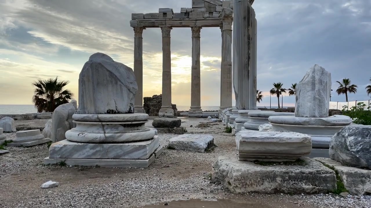 Turchia, Side, le enormi colonne del Tempio di Apollo al tramonto. Il filmato inizia con il suo riflesso e si inclina lentamente verso l'alto, palme dietro le colonne, nuvole bianche e il cielo che cambia colore. Rovine magnifiche