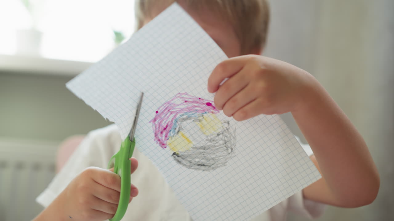 Søt gutt klipper ut fargelagt tegning av rutete papir i klassen.