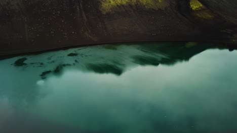 aerial view of a turquoise volcanic lake in the icelandic highlands mountains, on a cloudy day