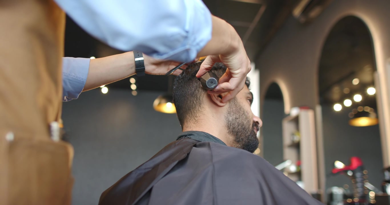 Posizionando pettine e rifinitore, un barbiere africano rifinisce le basette di un cliente in negozio per una sfumatura, con spazio per il testo.