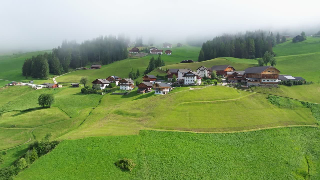 ubicadas en medio de campos verdes, las casas y granjas de val badia presentan un retrato tranquilo de la vida rural, con una suave manta de niebla que rueda suavemente en la distancia.