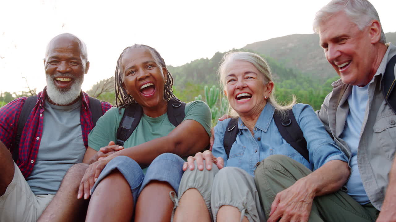 Portrait Of Active Senior Friends Sitting Taking A Break Hiking Through Countryside Together