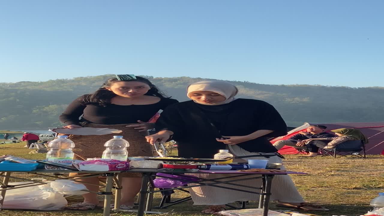 vertical footage, with friends camping and making breakfast of bread, sandwiches, sausages with a view of the clean Sermo reservoir.