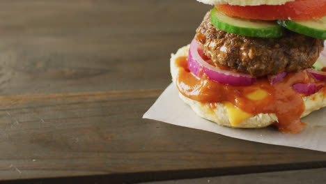 video of hamburger with salad and relish in burger bun on wooden table top, with copy space