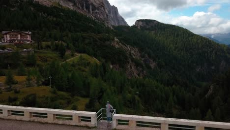 Lake-Fedaia-Dam-in-the-Dolomite-mountain-area-of-northern-Italy-with-a-person-admiring-view-from-the-railing-structure-near-Rifugio-Dolomia,-Aerial-Drone-flyover-view