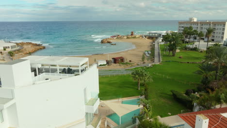 coastal scene in pernera, cyprus, with a view of a sandy cove, emerald waters, modern architecture, and a landscaped garden leading to the beach