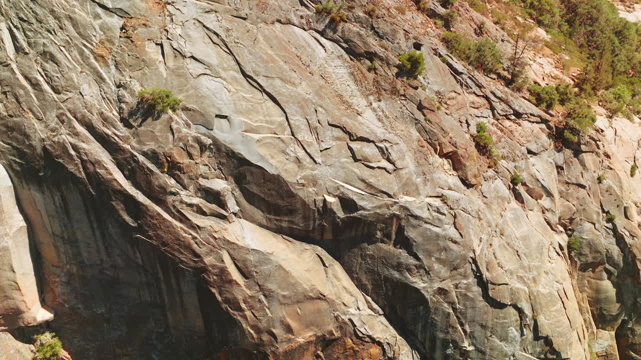 Close look at the bare grey rocks on sunny day. Huge cliff with rare greenery growing on the cliffs from top view.