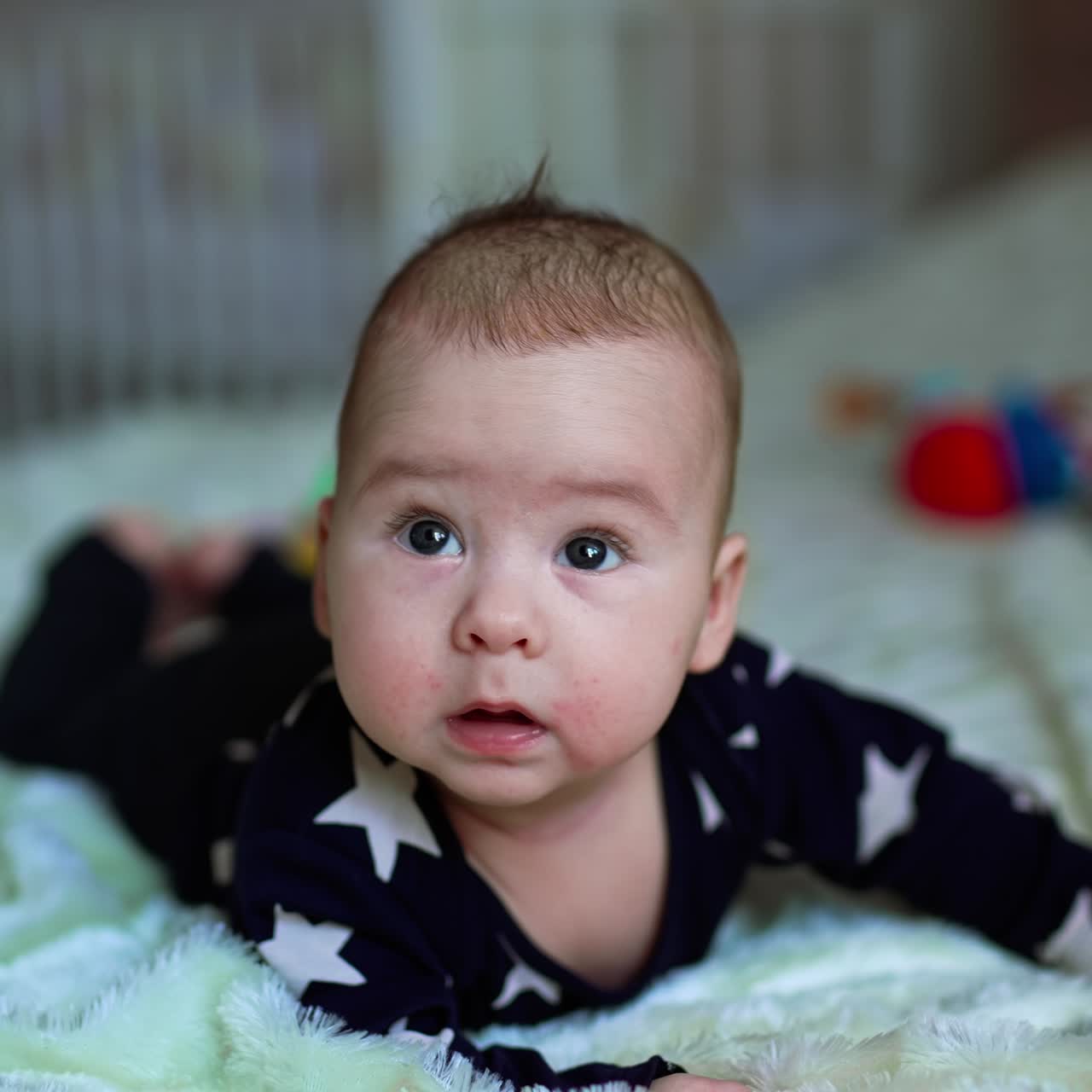 Beautiful little kid straightened his arms to look up with curiosity. Caucasian child in dark pajamas lies on belly on the bed