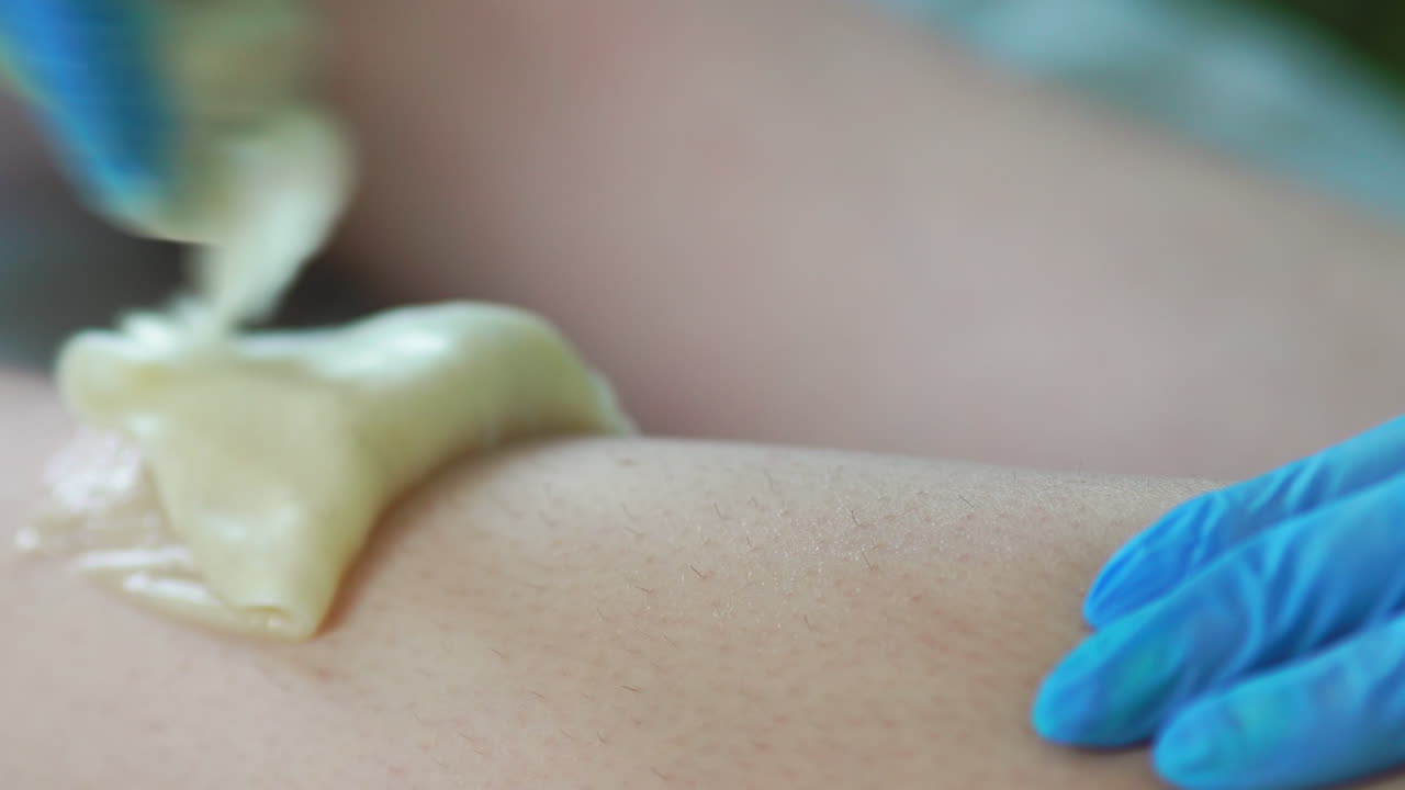 primer plano en el salón de belleza maestro en guantes haciendo el procedimiento para eliminar el vello en las piernas con una mezcla de azúcar