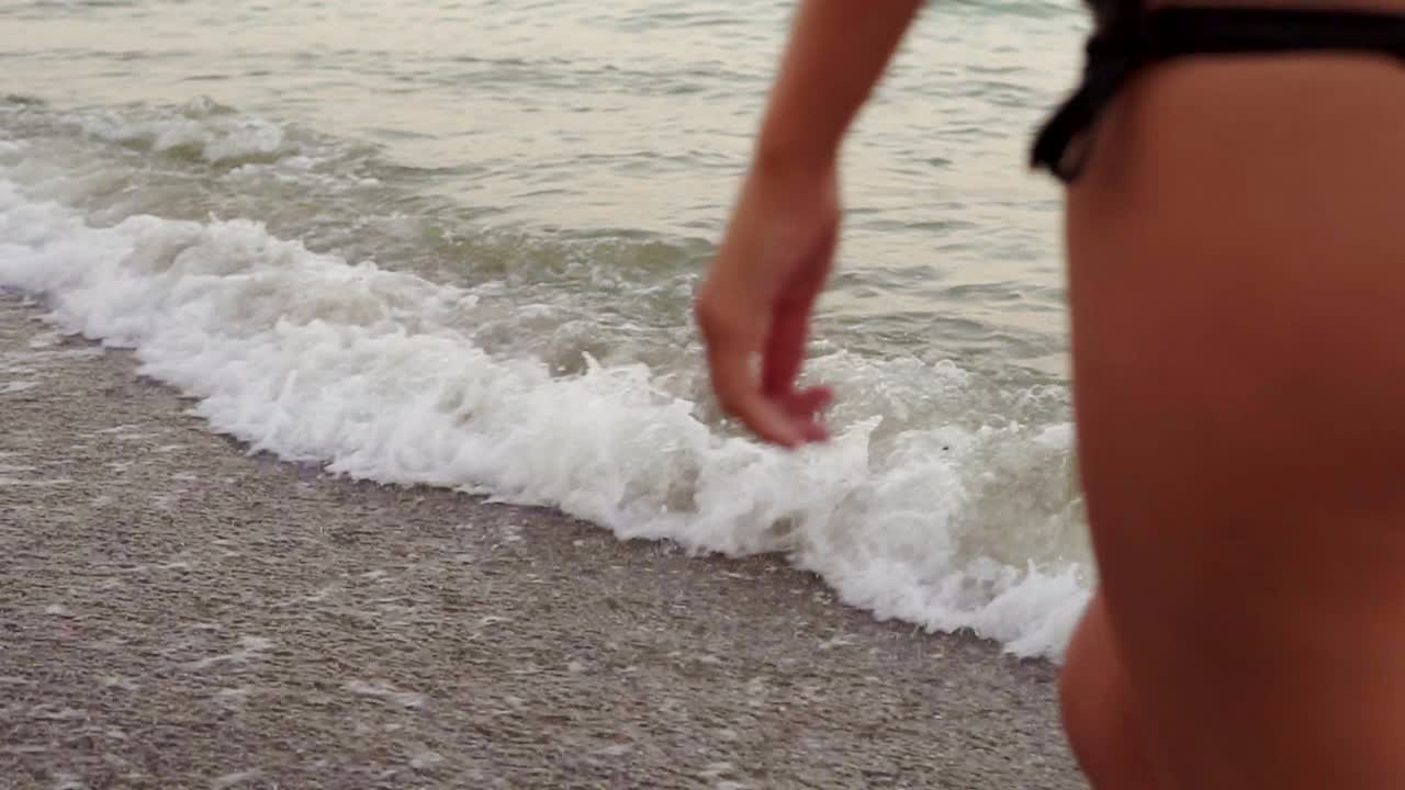 Close Up view sexy woman's back and legs walking by the water on the beach. Slow Motion shot