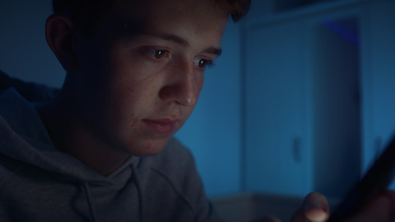 밤에 방에 앉아서  ⁇ 드폰을 사용하는 백인 십대 소년.