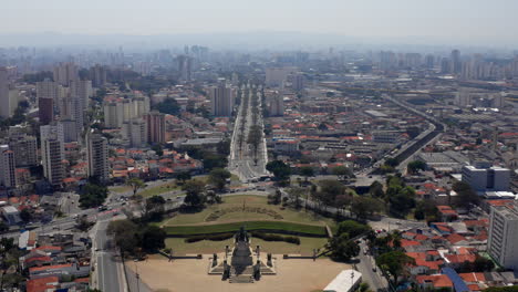 Drohne-Fliegt-Durch-Das-Unabhängigkeitsdenkmal-Im-Unabhängigkeitspark-Und-Enthüllt-Die-Avenue-Don-Pedro-I-Davor-Mit-Der-Stadt-São-Paulo-Im-Hintergrund