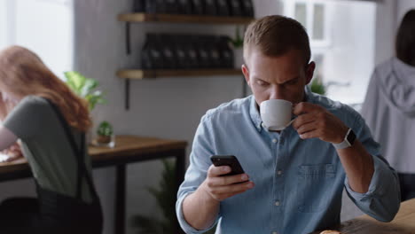 Junger-Geschäftsmann-Benutzt-Smartphone-Im-Café,-Trinkt-Kaffee-Und-Surft-Online,-Liest-E-Mails,-Schreibt-SMS-Auf-Dem-Mobiltelefon-Und-Sendet-SMS-Nachrichten.-Er-Genießt-Die-Kommunikation-über-Das-Mobiltelefon