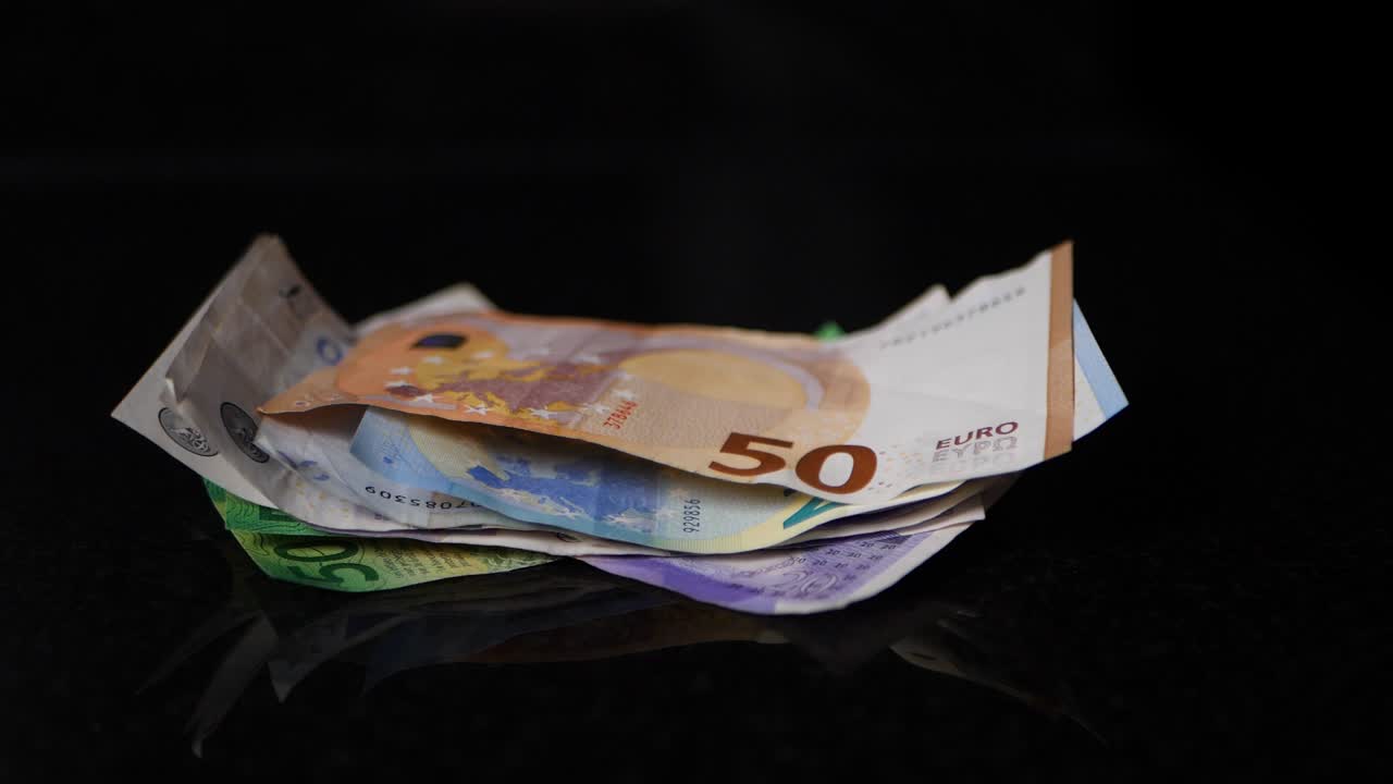 Seddelbundt med en 50 euro-seddel øverst falder i slow motion ned på en sort overflade.