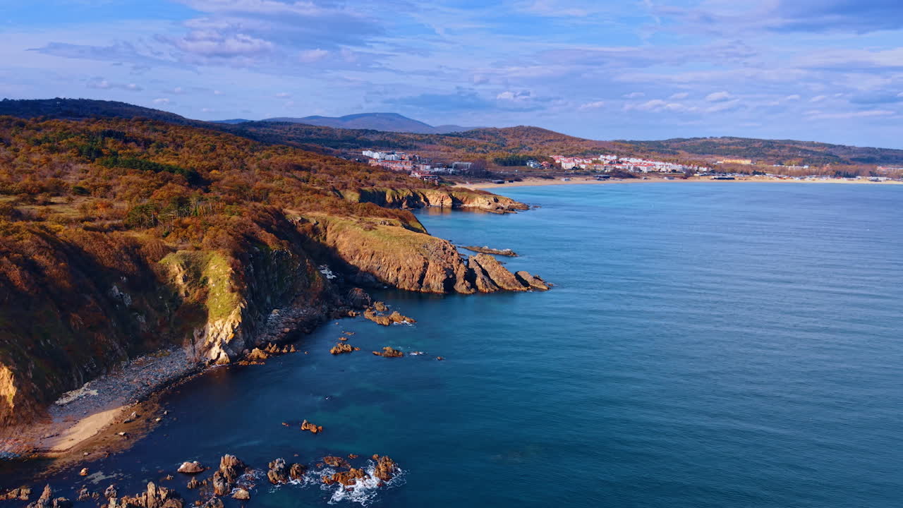 Autumn cliffs above calm sea bay. Rocky coastline with autumn hillsides and distant shoreline buildings