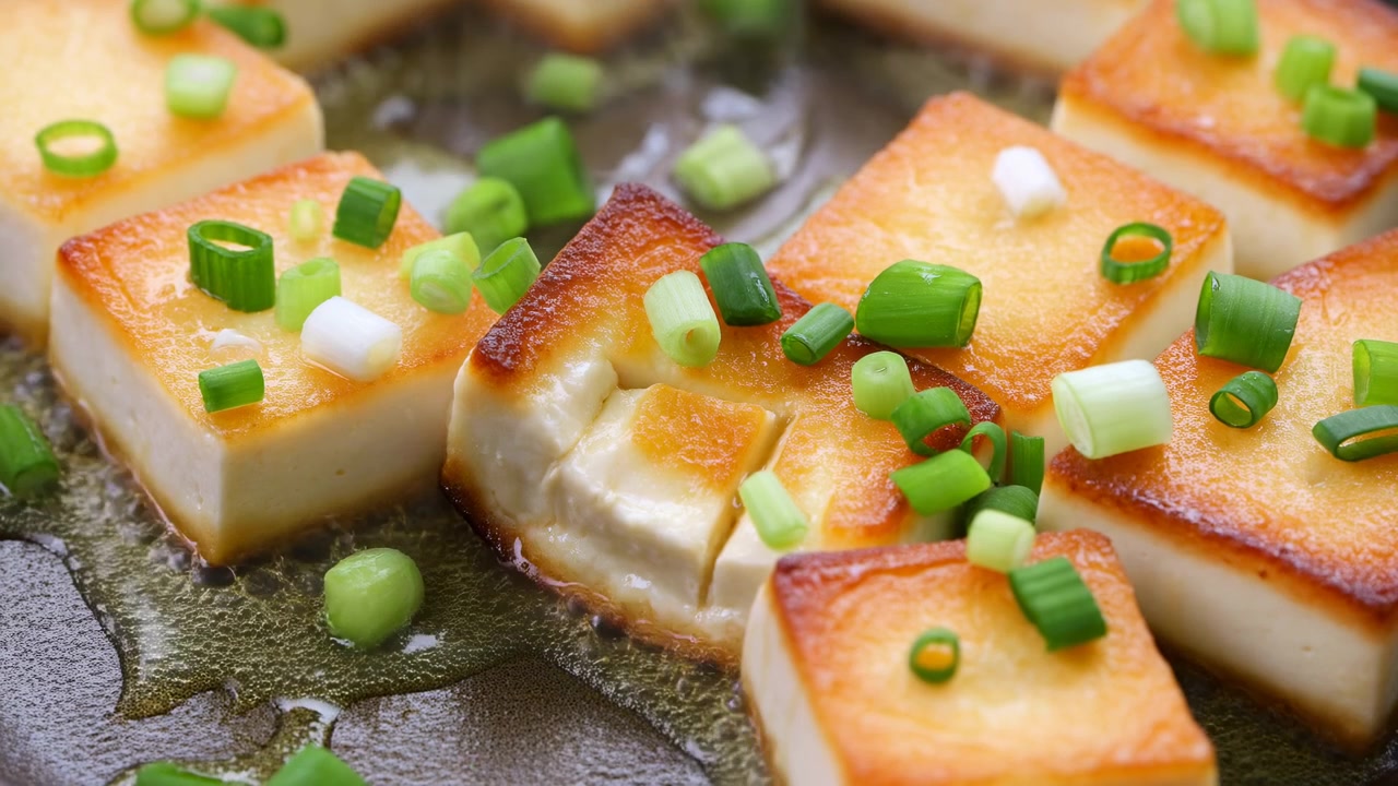 Cubes de tofu dorés poêlés avec oignons verts grésillant dans une poêle en fonte, bords caramélisés et sésame lustré