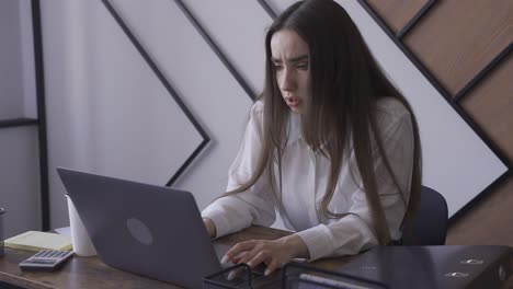 a woman is working with her laptop in an office. she reads something and she seems to be very preoccupied.