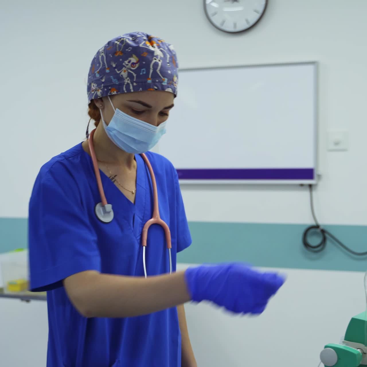 Young female doctor anesthesiologist with stethoscope hanging on her shoulders. Medic turns the handle on the equipment in surgery room