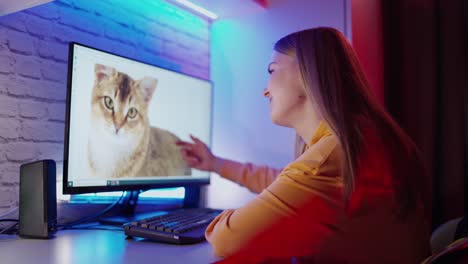 young girl looking at the screen of a computer. beautiful woman sitting at the table and touching the monitor with the cat image.