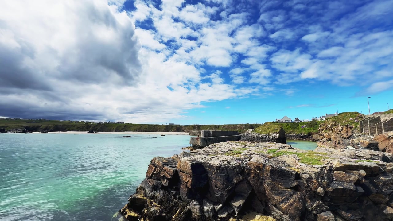 Vista costeira panorâmica no Porto de Ness, na Ilha de Lewis, nas Hébridas Exteriores da Escócia. Águas cristalinas e turquesa cercam uma costa rochosa sob nuvens dramáticas e céus azuis.