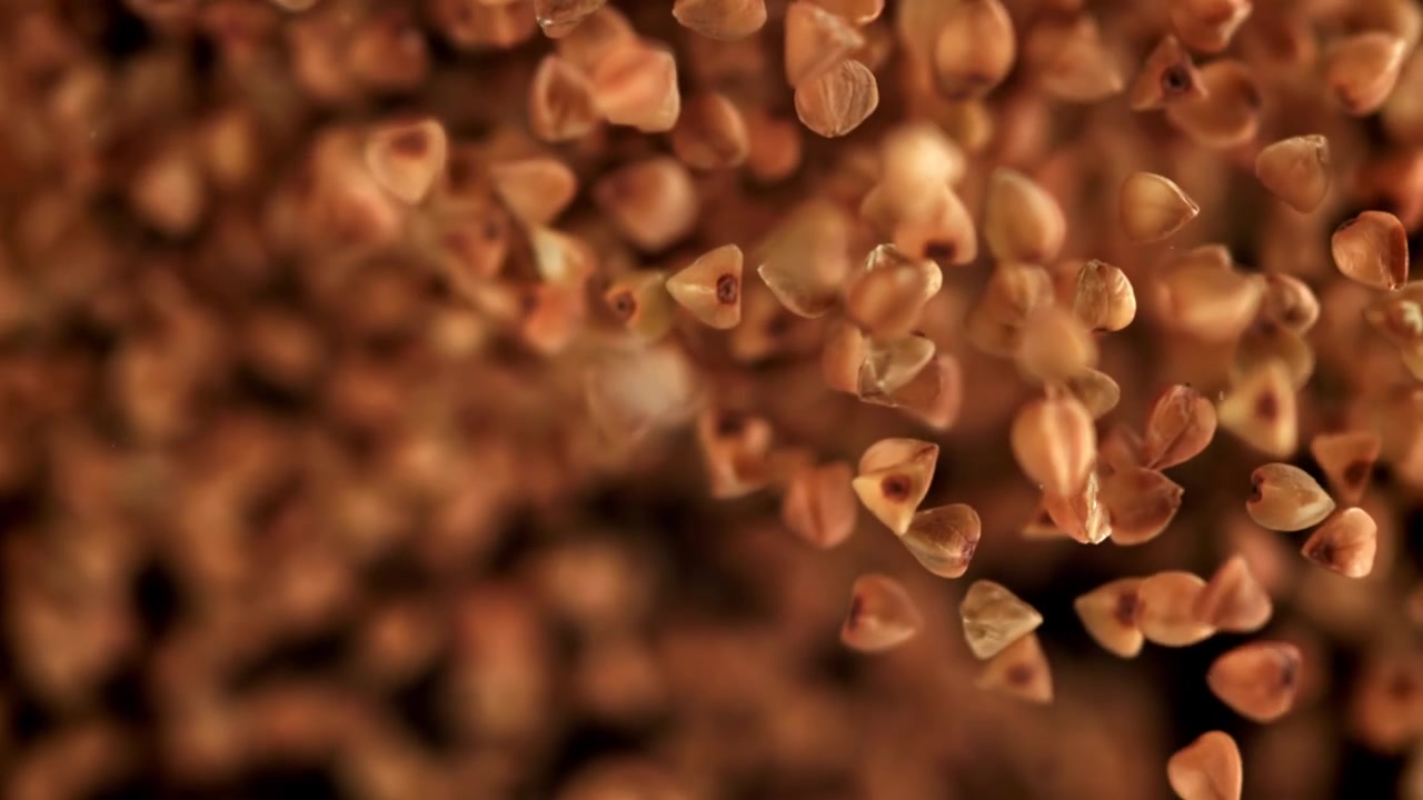 Grani di grano saraceno crudo in caduta al rallentatore su sfondo nero
