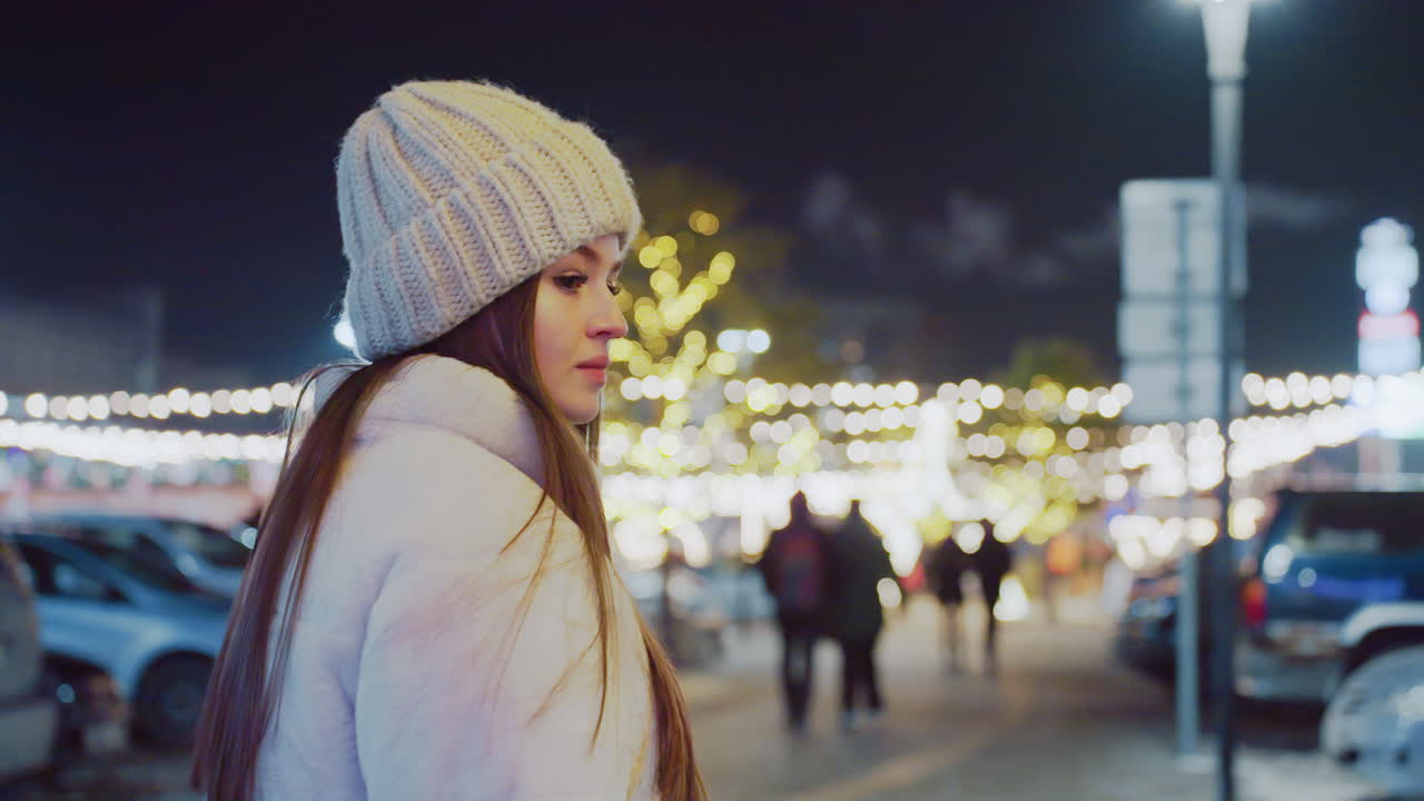 Woman in winter outfit and knitted beanie walking through vibrant city streets at night, surrounded by glowing festive lights and bokeh effects