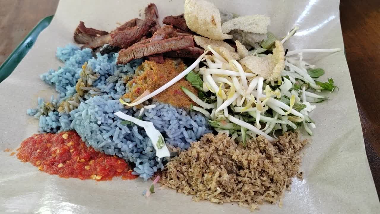 Nasi Kerabu, a traditional Malay dish from Kelantan, Malaysia, featuring blue rice, fresh herbs, and succulent grilled meat.