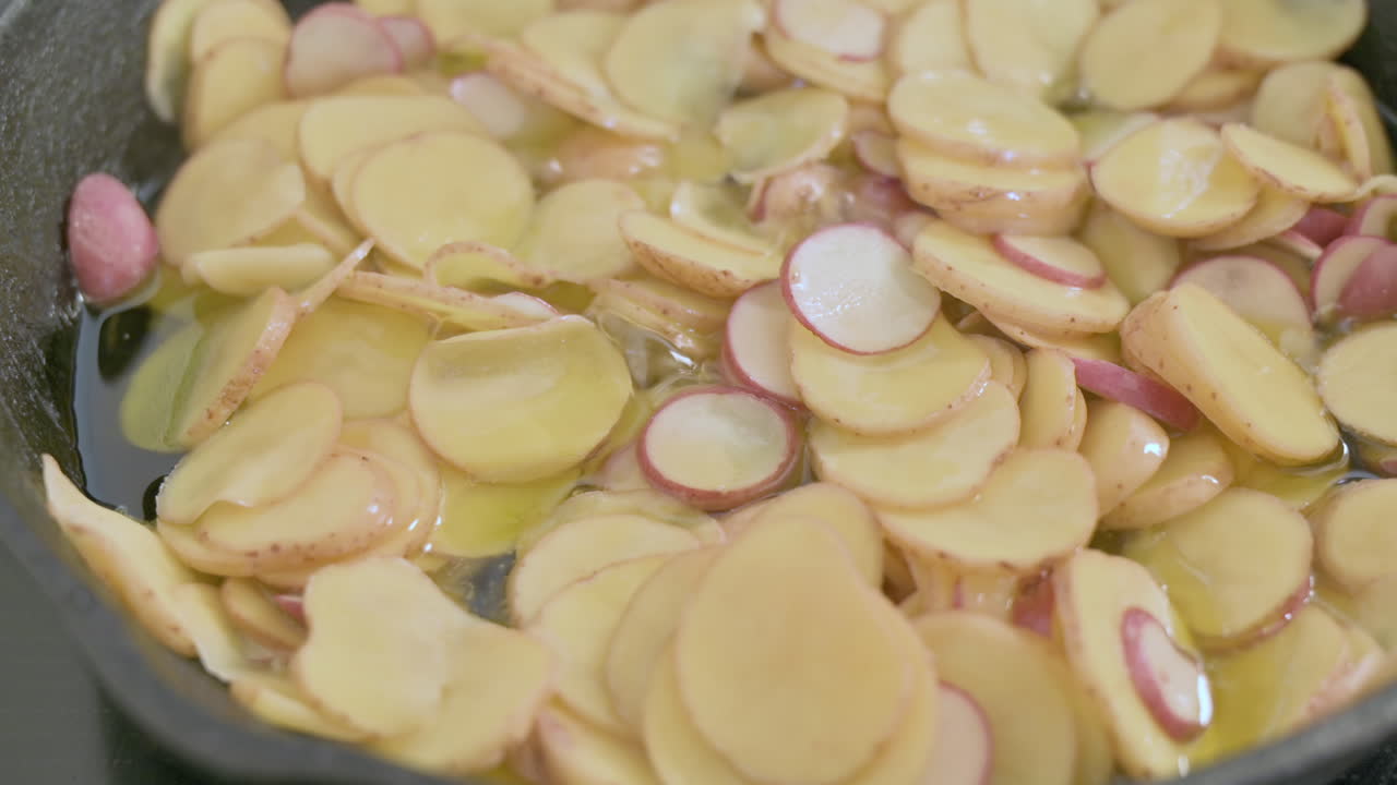 Patate a fette che cuociono in abbondante grasso in padella, ripresa statica ravvicinata.