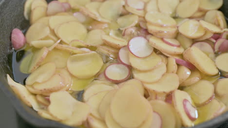 sliced potatoes cook in a lot of fat in pan, closeup static shot