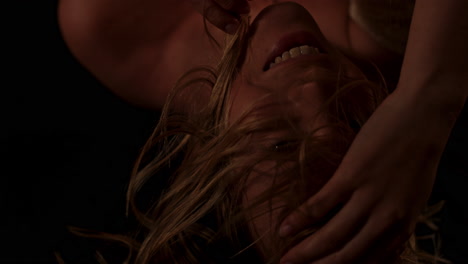 beautiful portrait of a happy, young woman sensually playing with her blonde hair in slow motion in a dark room