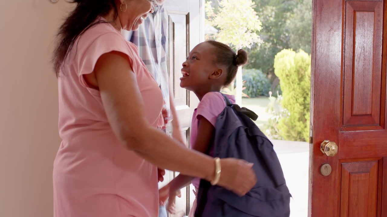 Granddaughter with backpack hugging welcoming diverse grandparents, morning, embrace, at home