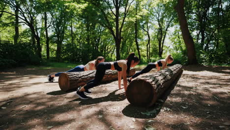 three women exercising on logs in a forest