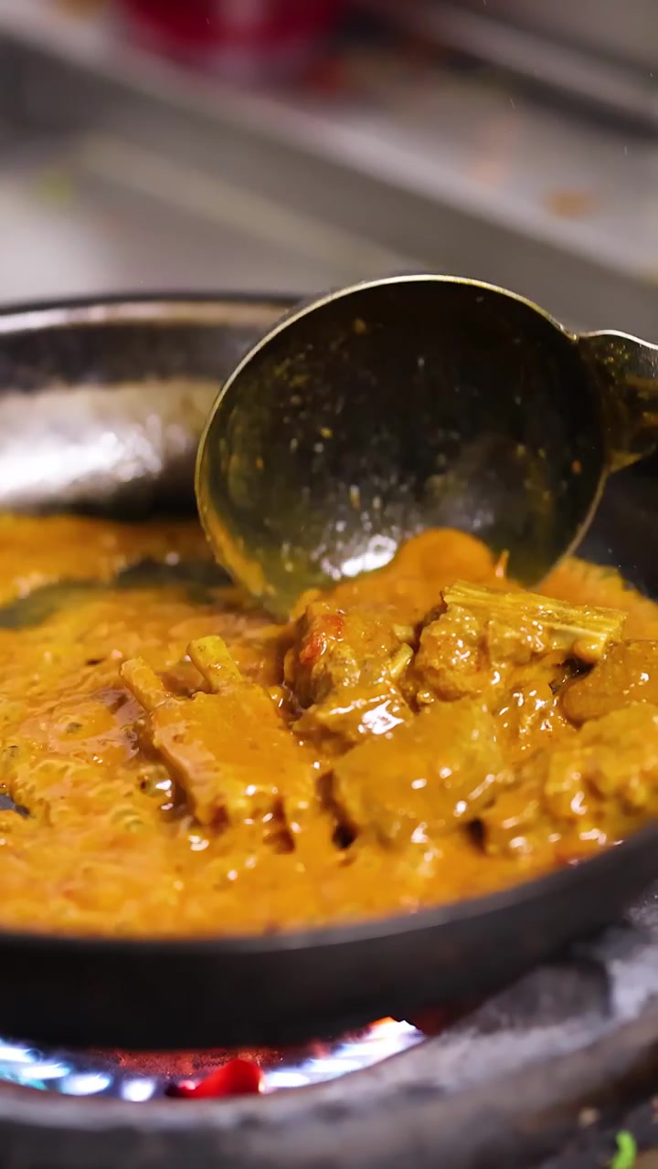 Primo piano di un mestolo di metallo che mescola salsa curry arancione in una padella calda.