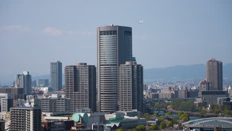 slow motion shot of an airplane disappearing behind a skyscraper in downtown osaka