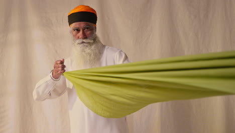 fotografía de estudio de un anciano sikh doblando tela para un turbante contra un fondo plano como secuencia parte 1 de 2