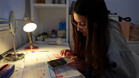 chica con gafas estudia haciendo operaciones con una calculadora científica por la noche