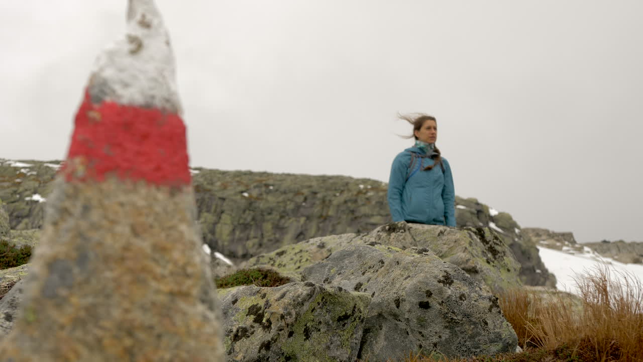 женщина стоит у указателя на туристической тропе в холодный, ветреный и пасмурный день