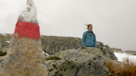 a woman stands by a trail marker on a hiking trail on a cold, windy and overcast day