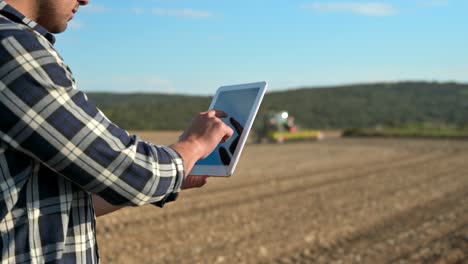 el agricultor lee o analiza un informe en una computadora tablet sobre el campo agrícola. el tractor en el fondo ara un campo. agricultura inteligente utilizando tecnologías modernas. estilo de vida en la agricultura. imágenes de alta calidad en 4k