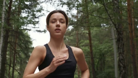 determined young woman wearing sport top running in forest in morning