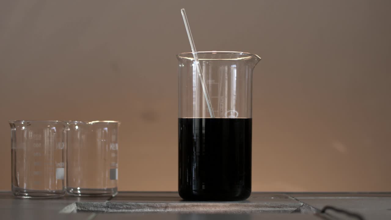 어두운 액체는 는 막대기와 시험 튜브와 함께 컵에 넣습니다.