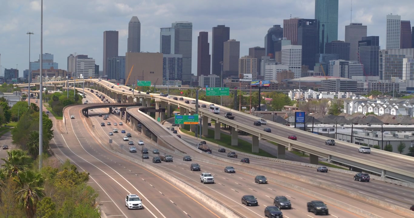 This drone view captures the downtown Houston, Texas skyline alongside the I 45 South freeway, with cars moving along the busy highway corridor.